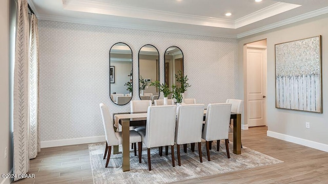 dining space featuring a tray ceiling, ornamental molding, and light hardwood / wood-style floors