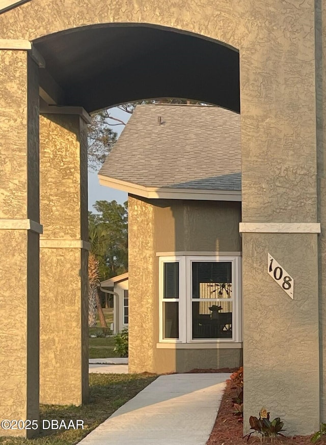 view of exterior entry featuring stucco siding and a shingled roof