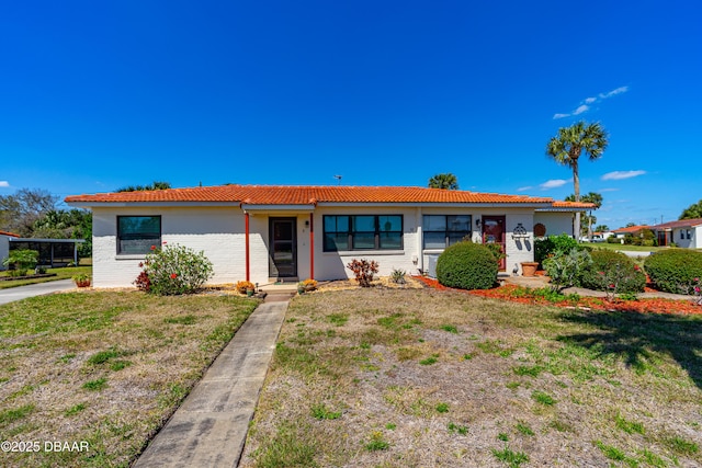 ranch-style home featuring brick siding, a front yard, and a tile roof