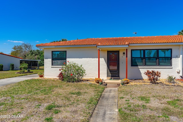 view of front of home with a front lawn, a tiled roof, and brick siding