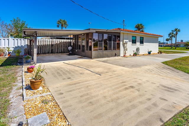 view of front of home featuring fence, concrete driveway, a sunroom, an attached carport, and brick siding