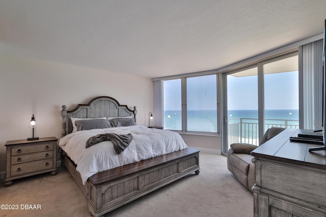 bedroom featuring access to outside, light colored carpet, a textured ceiling, and a water view