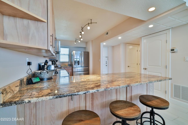 kitchen featuring kitchen peninsula, light brown cabinetry, stainless steel fridge with ice dispenser, and light stone countertops