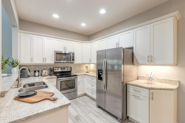 kitchen featuring white cabinets, sink, light stone countertops, light wood-type flooring, and stainless steel appliances