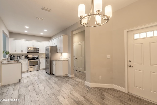 kitchen with light wood-type flooring, stainless steel appliances, pendant lighting, a notable chandelier, and white cabinetry