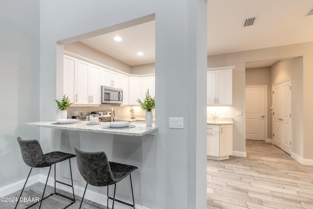 kitchen with kitchen peninsula, light stone countertops, white cabinets, light hardwood / wood-style floors, and a breakfast bar area