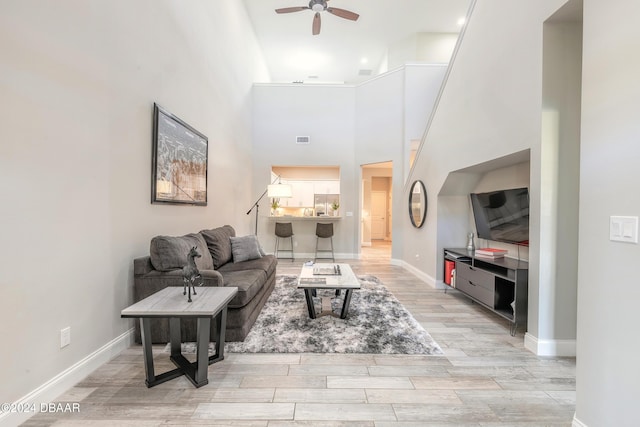 living room with ceiling fan, light hardwood / wood-style floors, and a towering ceiling