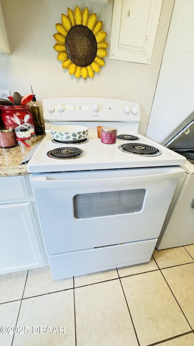 kitchen with white electric stove, light tile patterned floors, and white cabinets