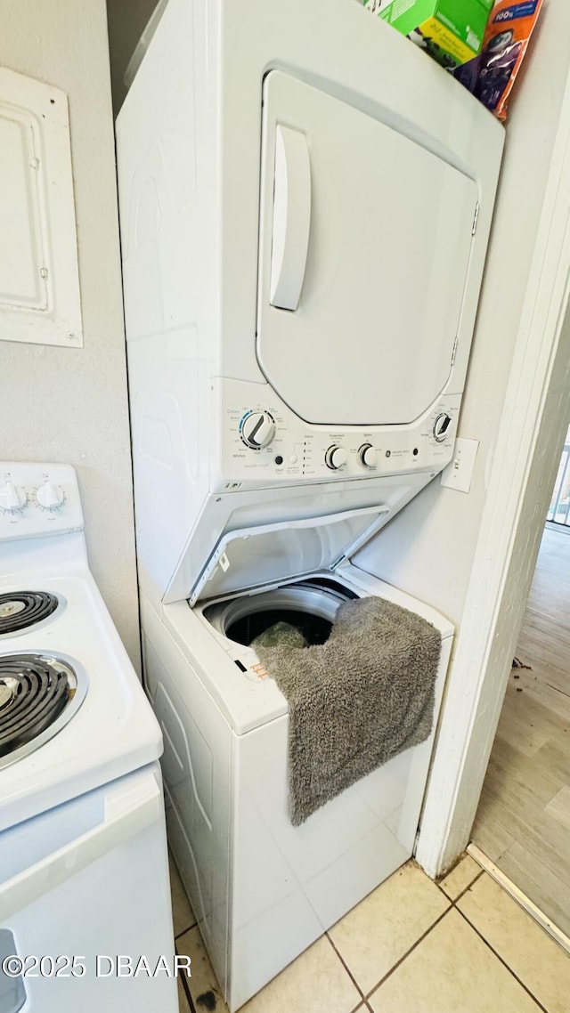 washroom with stacked washer and clothes dryer, light tile patterned floors, and electric panel