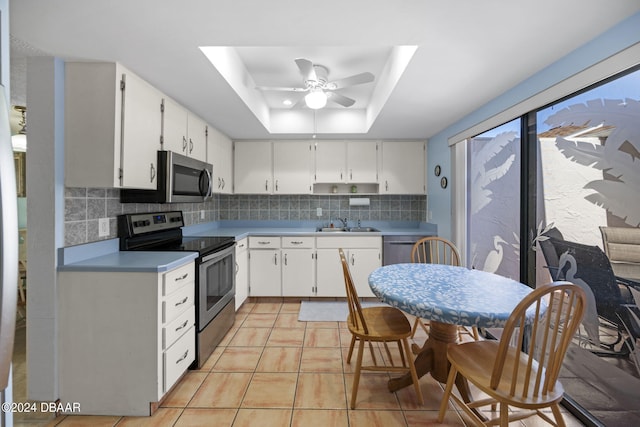 kitchen with sink, a raised ceiling, stainless steel appliances, decorative backsplash, and white cabinets