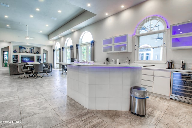 kitchen with wine cooler, a high ceiling, ceiling fan, and white cabinets