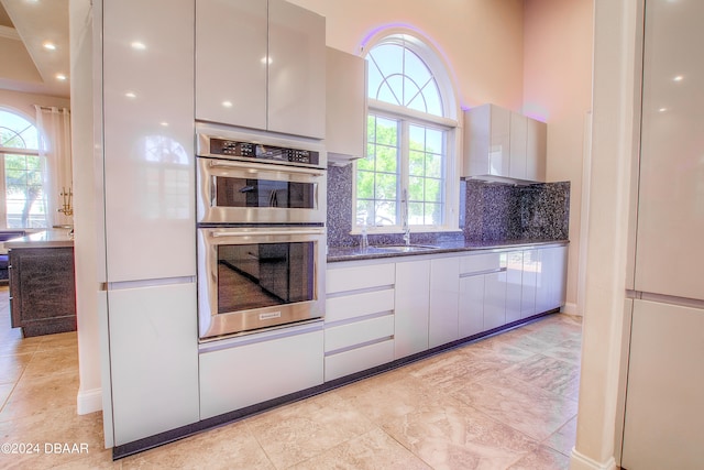 kitchen featuring dark stone counters, white cabinetry, decorative backsplash, and double oven