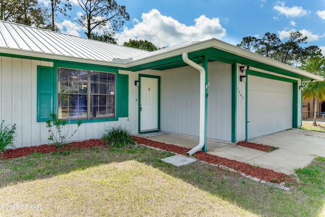 ranch-style house featuring concrete driveway, an attached garage, metal roof, and a front yard