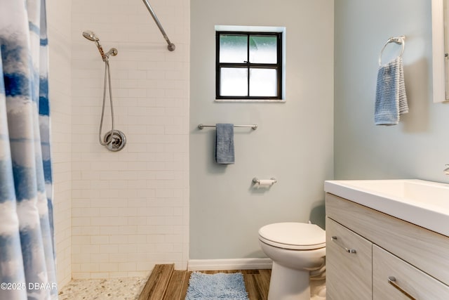 bathroom featuring a tile shower, toilet, vanity, and wood finished floors