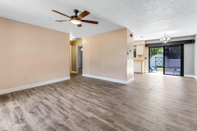 unfurnished living room with wood finished floors, a textured ceiling, baseboards, and ceiling fan with notable chandelier