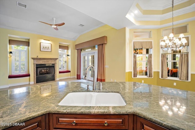 kitchen with sink, stone countertops, hanging light fixtures, ornamental molding, and a raised ceiling