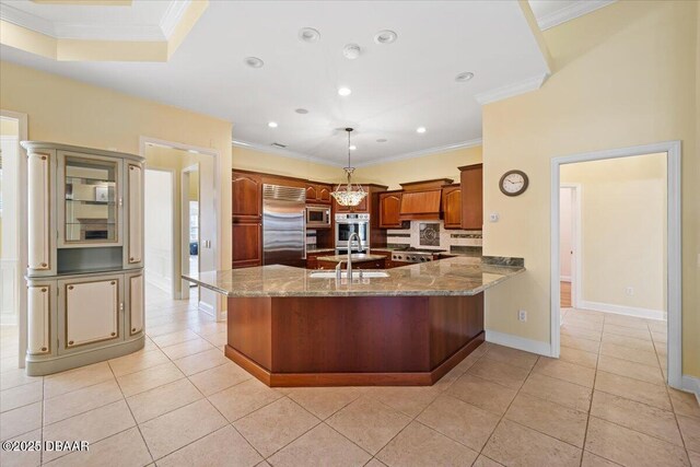 kitchen with pendant lighting, sink, stone counters, built in appliances, and kitchen peninsula