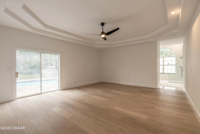 spare room with a tray ceiling, light hardwood / wood-style flooring, and ceiling fan