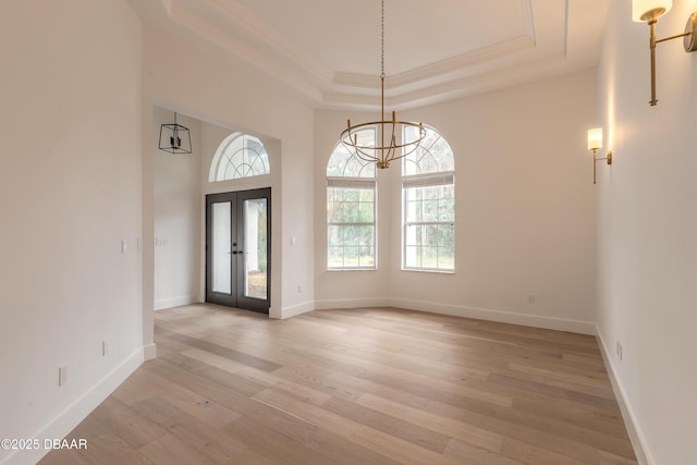 interior space with a raised ceiling, crown molding, a chandelier, and light hardwood / wood-style floors