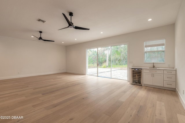 unfurnished living room featuring ceiling fan, beverage cooler, light hardwood / wood-style flooring, and wet bar