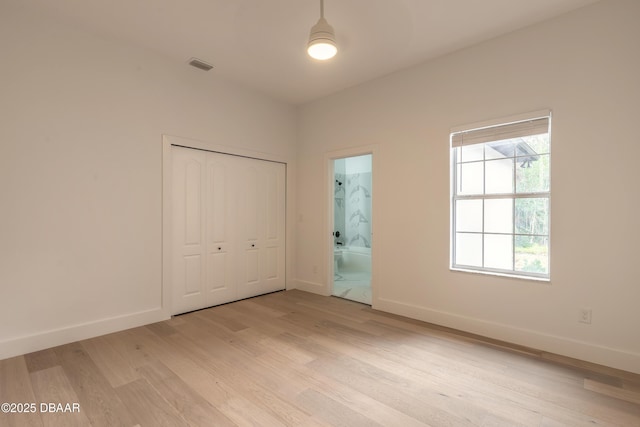 unfurnished bedroom featuring ensuite bathroom, a closet, and light wood-type flooring