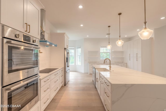 kitchen with appliances with stainless steel finishes, white cabinetry, hanging light fixtures, a spacious island, and light stone counters