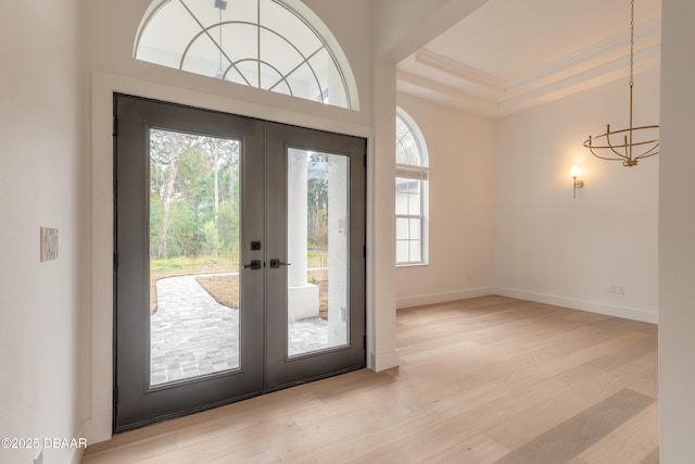 doorway to outside with french doors, ornamental molding, a raised ceiling, and light hardwood / wood-style floors