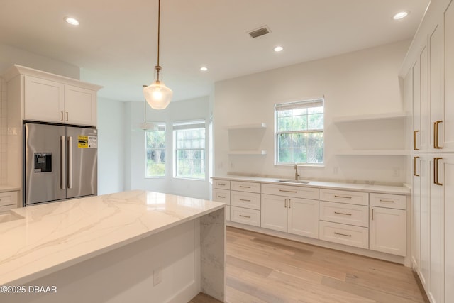 kitchen featuring sink, light stone counters, hanging light fixtures, stainless steel fridge, and white cabinets