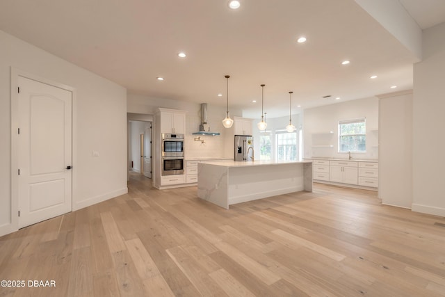 kitchen with appliances with stainless steel finishes, pendant lighting, white cabinets, wall chimney range hood, and a spacious island