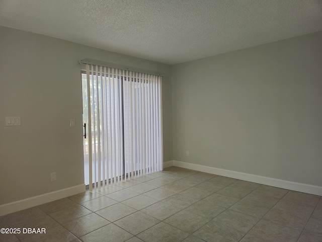 tiled spare room featuring a textured ceiling and baseboards