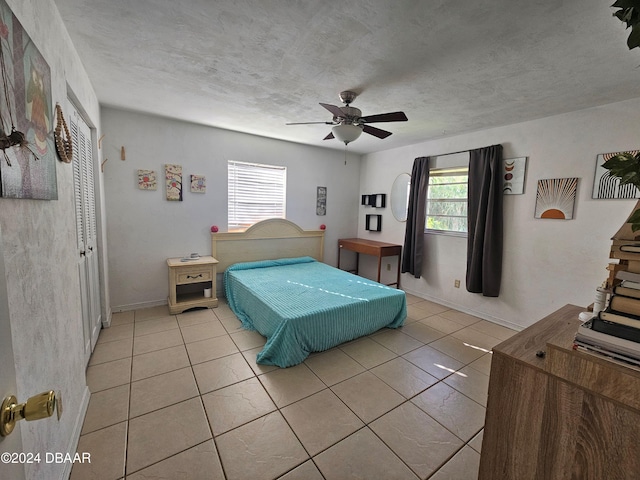 bedroom featuring a closet, a textured ceiling, light tile patterned flooring, and a ceiling fan