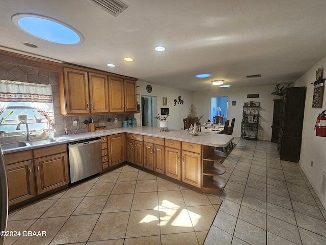 kitchen featuring stainless steel dishwasher, a peninsula, light tile patterned floors, and a sink