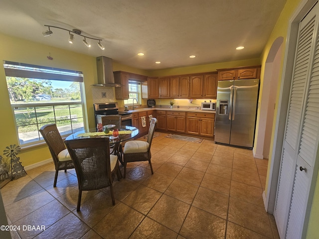 kitchen with recessed lighting, arched walkways, a sink, appliances with stainless steel finishes, and wall chimney exhaust hood