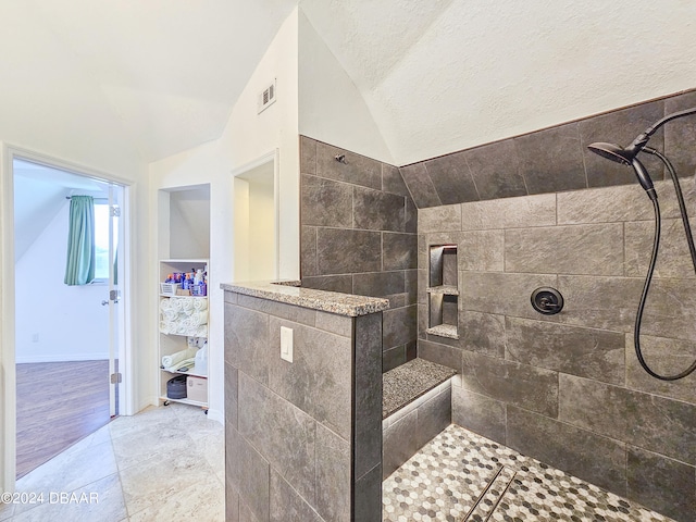 bathroom with a textured ceiling, lofted ceiling, hardwood / wood-style flooring, and a tile shower