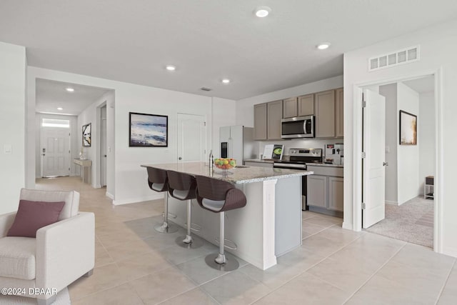 kitchen with stainless steel appliances, a kitchen breakfast bar, a kitchen island with sink, light stone counters, and light tile patterned floors