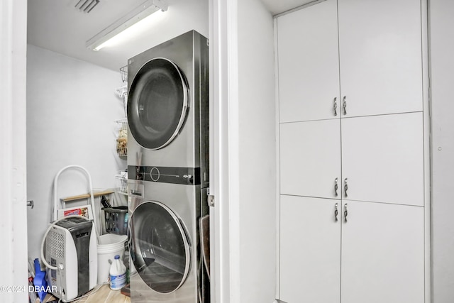 washroom with stacked washer / dryer, cabinets, and hardwood / wood-style flooring