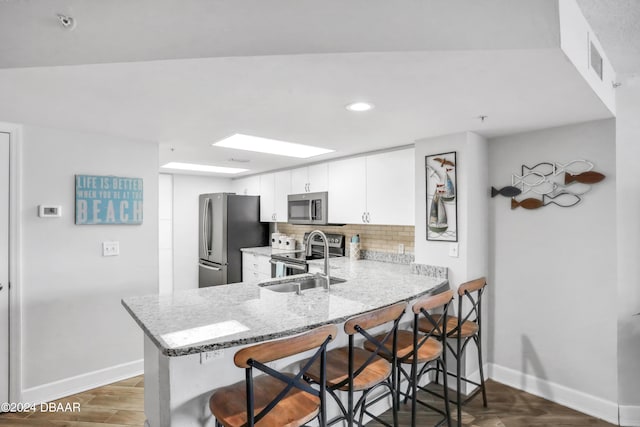 kitchen featuring kitchen peninsula, light stone countertops, white cabinetry, and appliances with stainless steel finishes