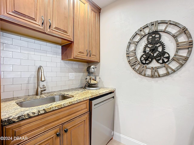 kitchen with dishwasher, light stone counters, a sink, and tasteful backsplash