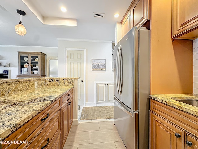 kitchen with light stone counters, brown cabinets, crown molding, decorative light fixtures, and freestanding refrigerator