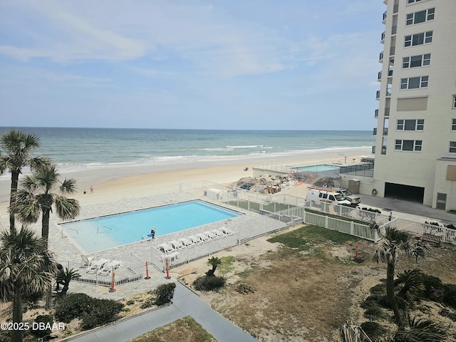 community pool featuring fence, a water view, and a beach view