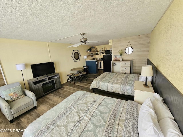 bedroom featuring wood finished floors, a textured ceiling, ceiling fan, a textured wall, and fridge