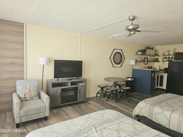 bedroom with freestanding refrigerator, a textured ceiling, ceiling fan, and wood finished floors