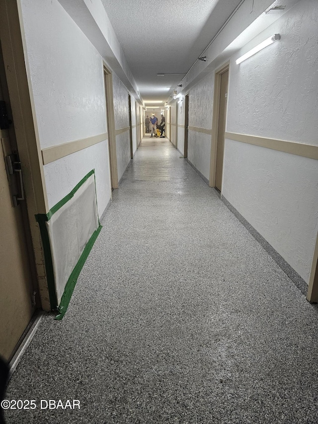 hallway featuring a textured ceiling, a textured wall, and speckled floor