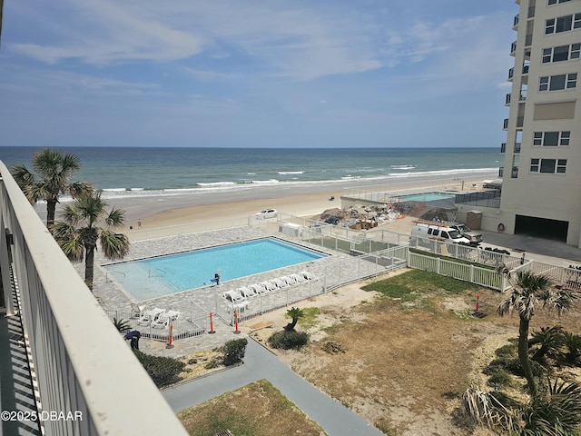 community pool with fence, a water view, and a beach view