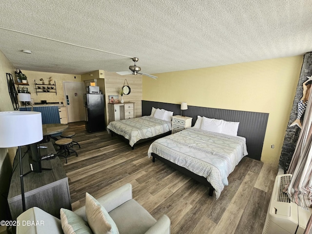 bedroom featuring freestanding refrigerator, a textured ceiling, ceiling fan, and wood finished floors