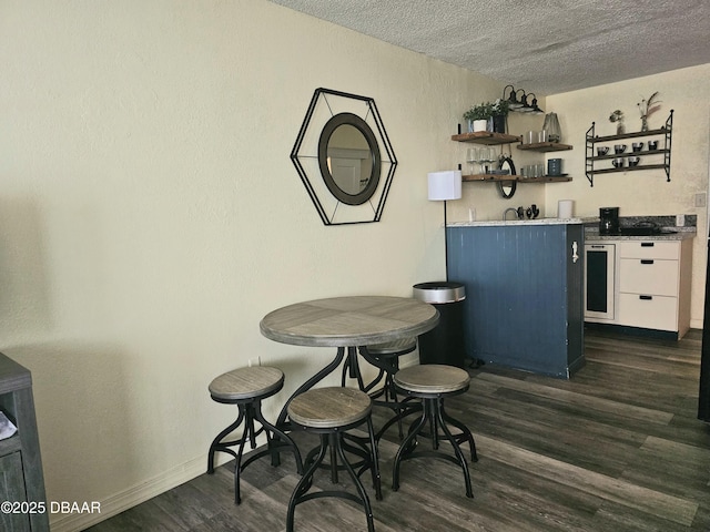 dining area with dark wood finished floors, wet bar, a textured ceiling, and baseboards