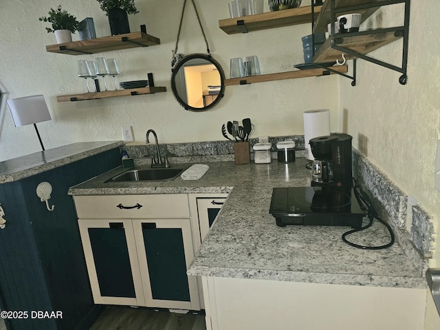 kitchen with open shelves, a textured wall, white cabinets, and a sink