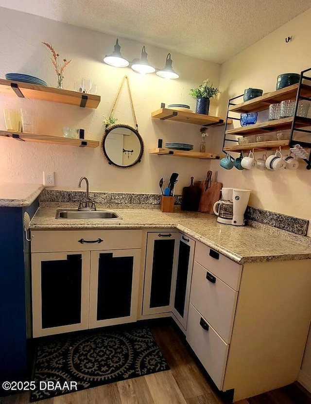 kitchen with white cabinets, sink, light stone countertops, a textured ceiling, and dark hardwood / wood-style flooring