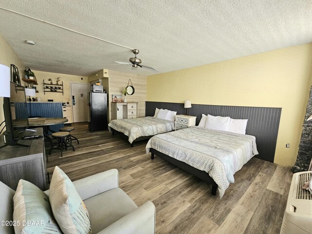 bedroom with freestanding refrigerator, a textured ceiling, ceiling fan, and wood finished floors
