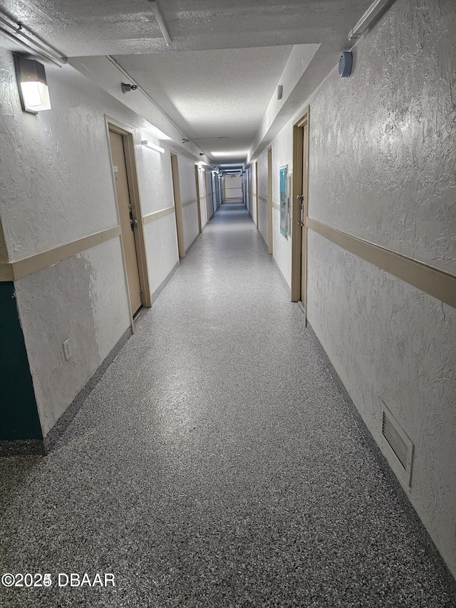 hallway with speckled floor, visible vents, and a textured wall